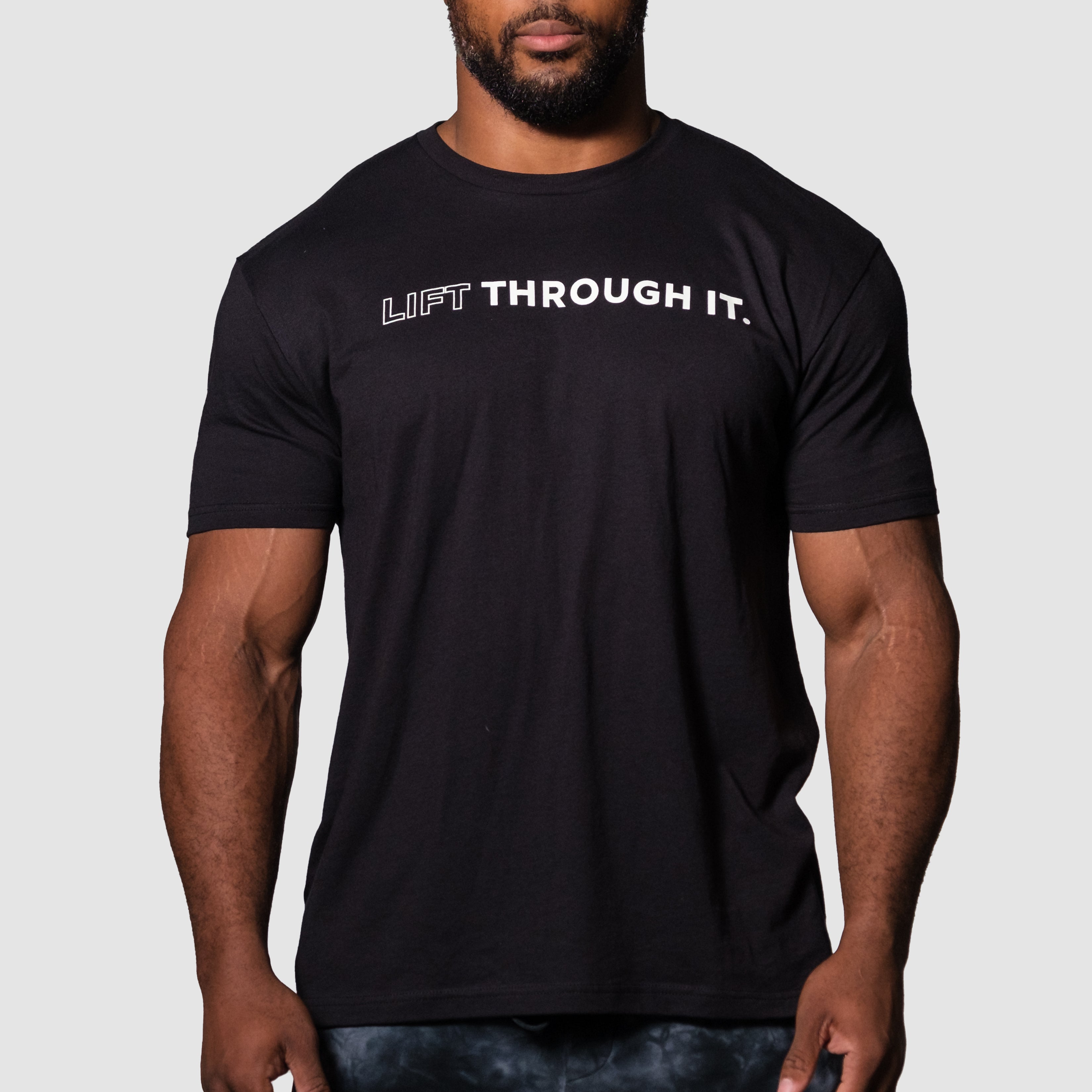 Model wearing the LTI Statement Performance Tee in black, featuring the text 'LIFT THROUGH IT.' on the front.