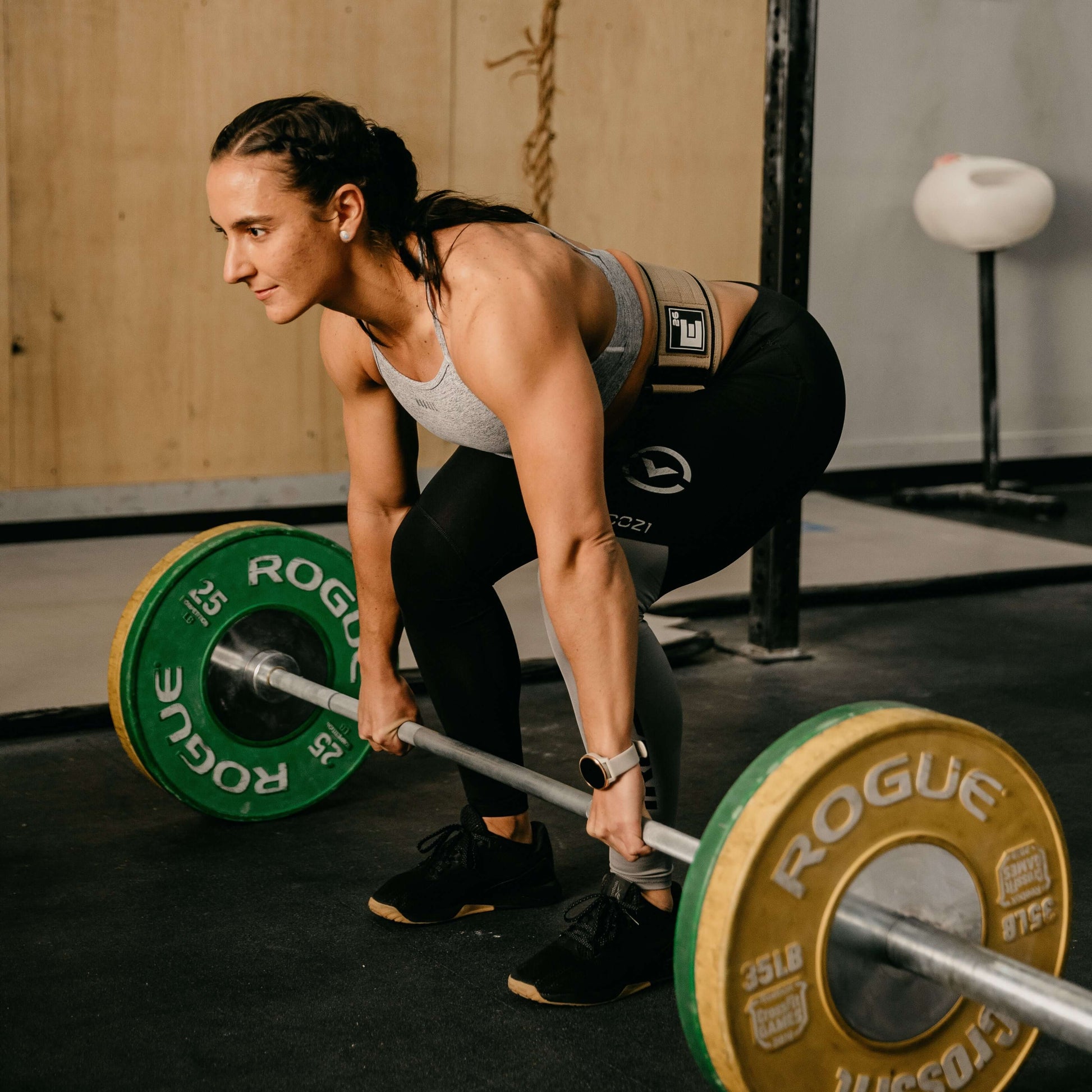 Woman using Self Locking Weightlifting Belt while performing deadlift with weights in gym.