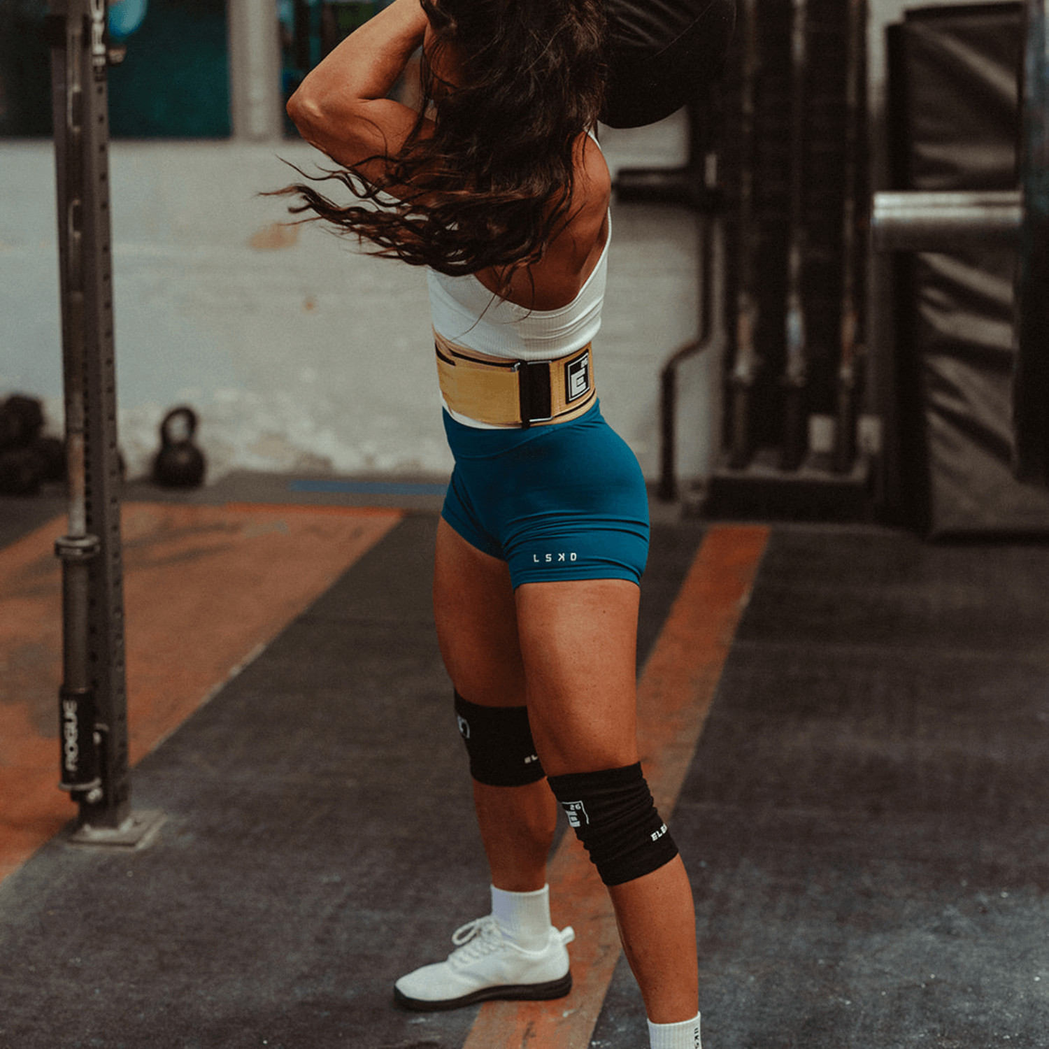 Woman lifting weights while wearing 3mm Agility Knee Sleeves in a gym setting.