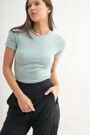 Model wearing MONO B Essential Micro-ribbed Cropped Athleisure Tee in light blue with high-waisted black pants.