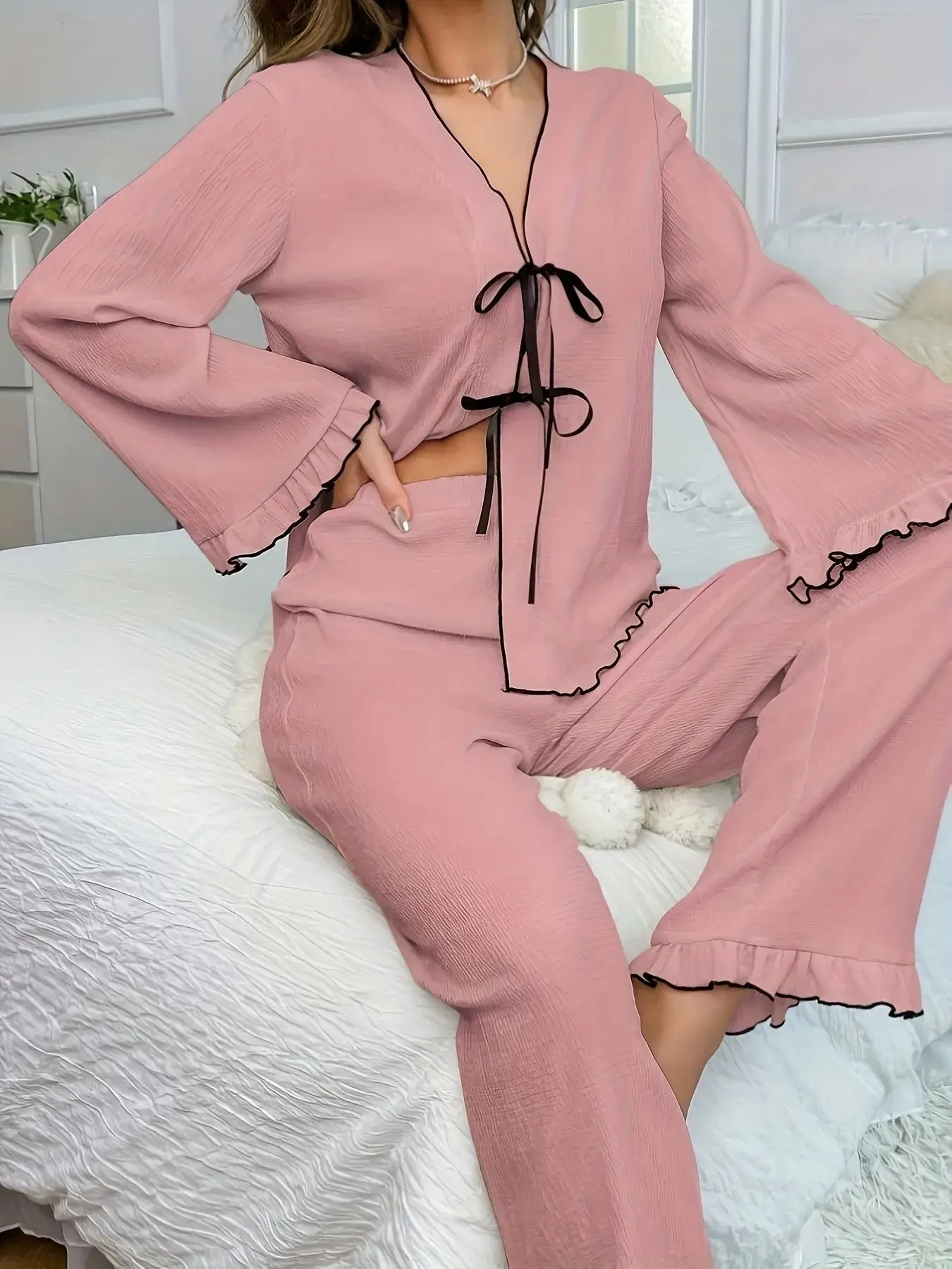 Frill Trim Bow Tie Shirt and Pants Lounge Set in pink, featuring bell sleeves and a tie detail, shown on a model sitting on a bed.