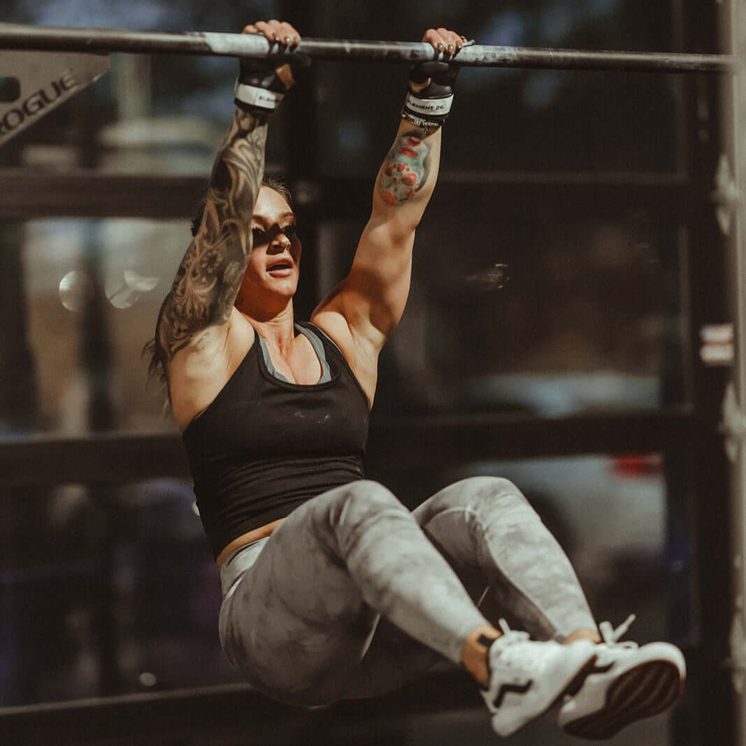 Woman performing a pull-up using Isocomp Gymnastic Hand Grips, showcasing strength and control.