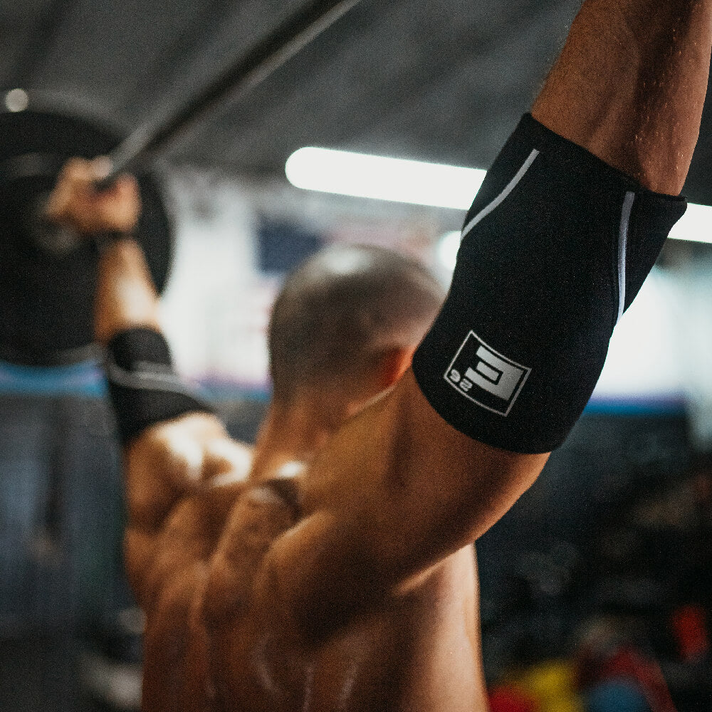 Athlete using 5mm Elbow Sleeves during an overhead lift in a gym.