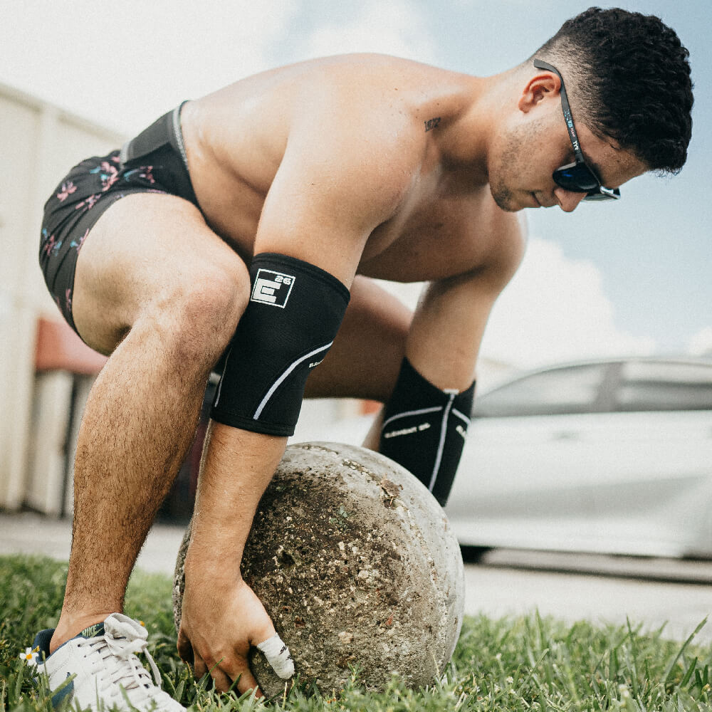 Athlete wearing 5mm Elbow Sleeves while lifting a stone ball outdoors, showcasing support and mobility.