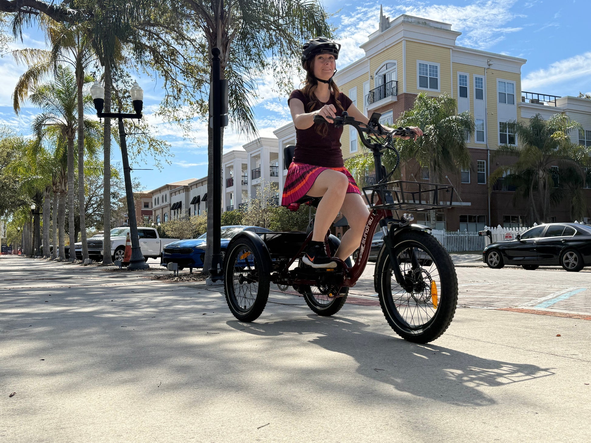 Woman riding the ONE-TRIKE 2.0 City Ebike on a sunny street with palm trees.