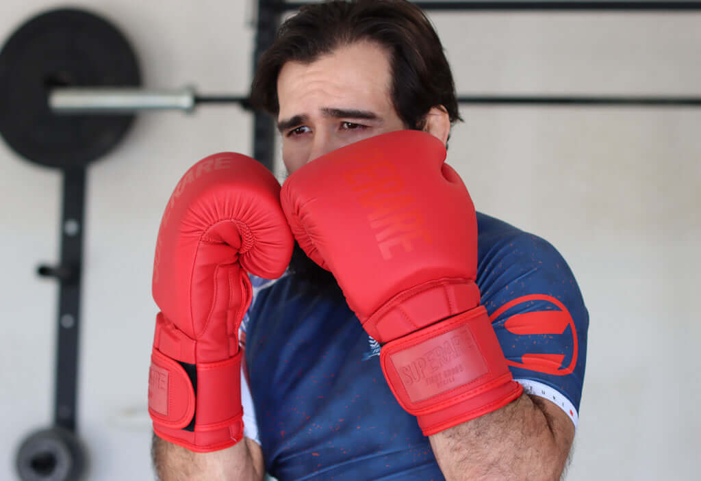 Man wearing Superare Supergel V Boxing Gloves in red, preparing to box at a gym.