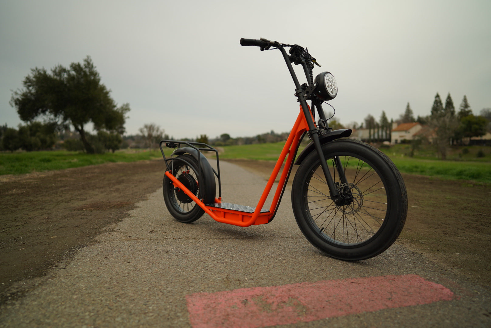EUNORAU JUMBO ELECTRIC SCOOTER in orange color parked on a gravel path surrounded by greenery and trees.