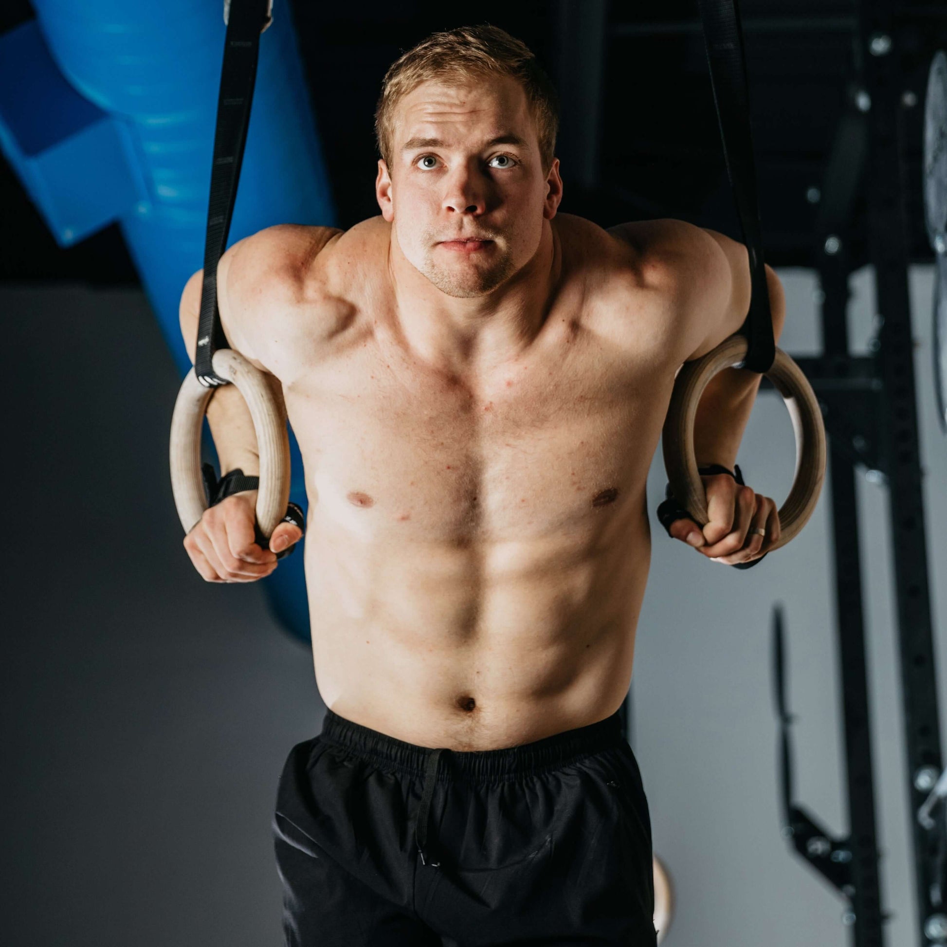 Isogrip Gymnastic Hand Grips used by a muscular athlete performing ring dips in a gym.