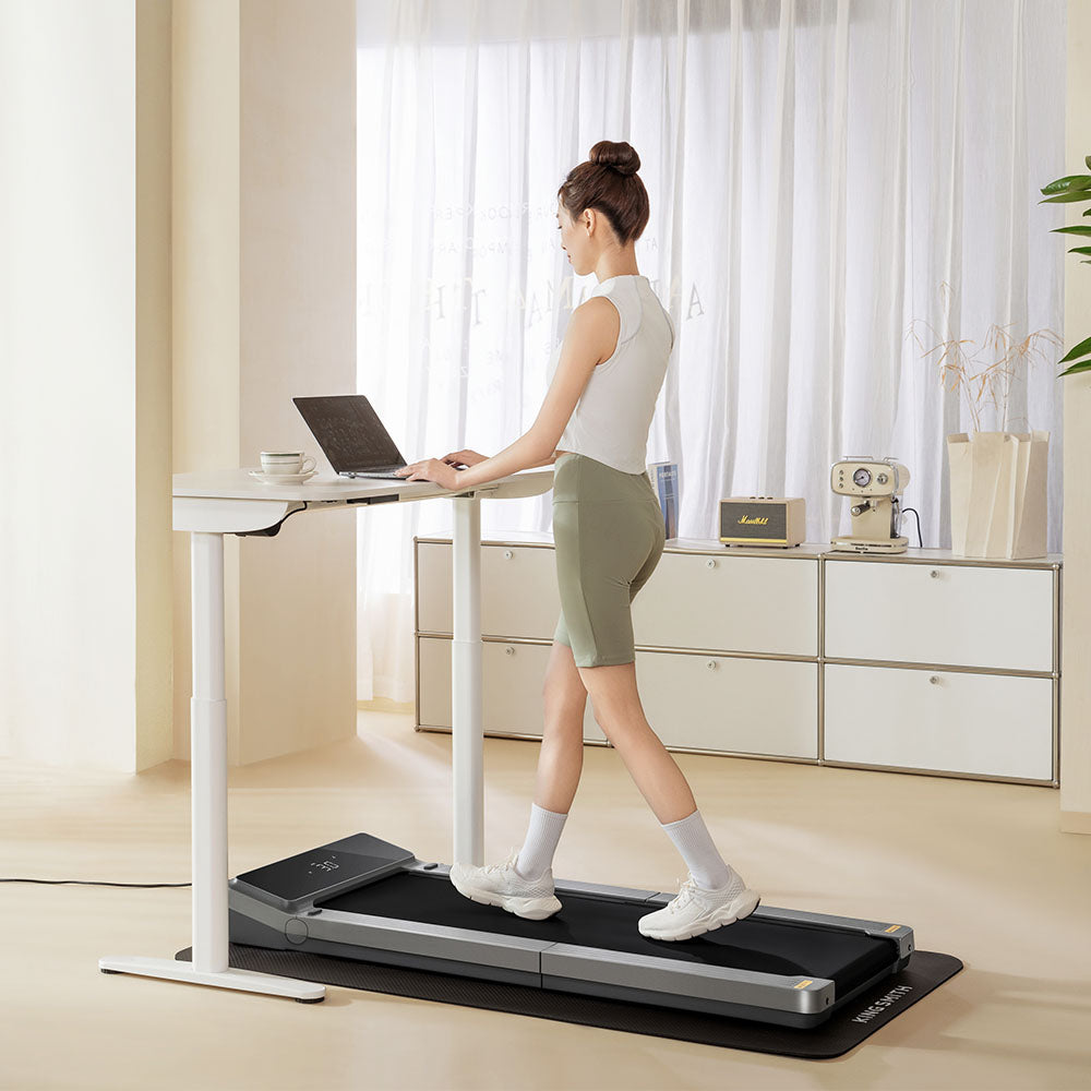 Woman using WalkingPad Z3 Just Walk Foldable Treadmill while working at a standing desk in a stylish home office.
