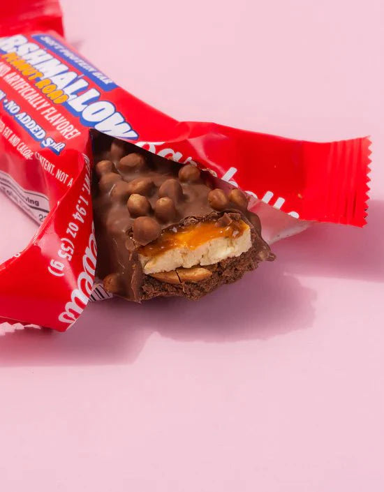 Close-up of a Barebells Soft Protein Bar with chocolate coating and a gooey filling on a pink background.