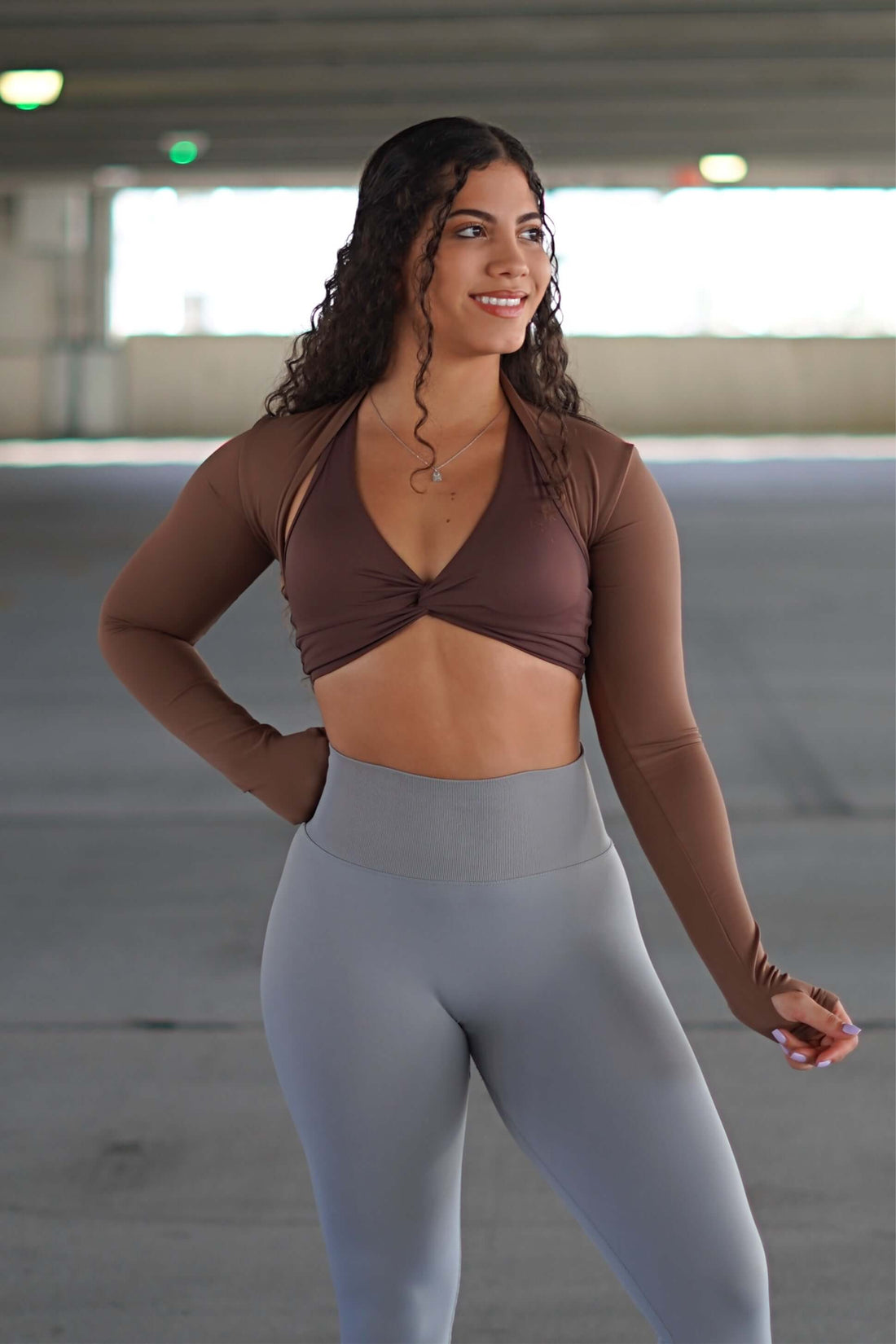 Model wearing Long Sleeve Bolero - Light Brown over workout attire in a parking garage.